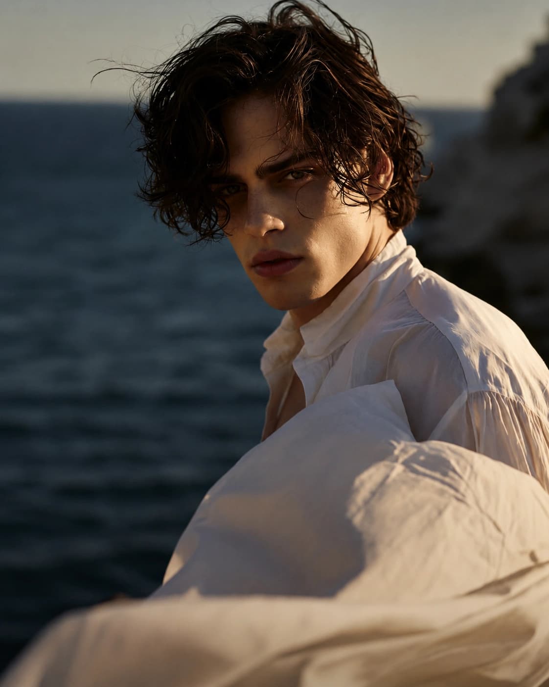 Portrait at the shoreline in late golden light, white shirt catching the wind.